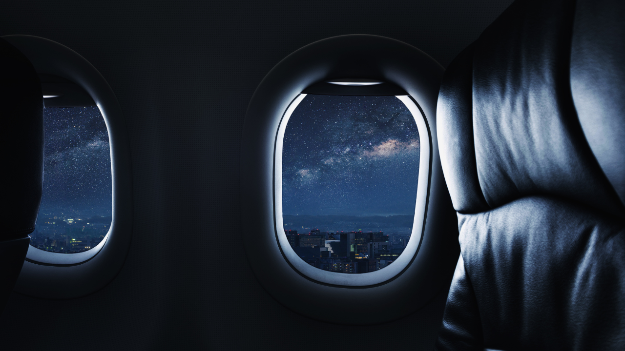 Airplane window overlooking a nighttime city skyline and star-filled sky, representing overnight travel and red-eye flight essentials.